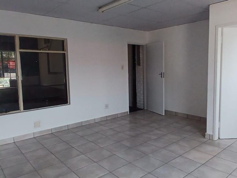 An empty, functional office space featuring neutral tiled flooring, white walls, and aluminium window frames, suitable for various industrial or commercial uses.