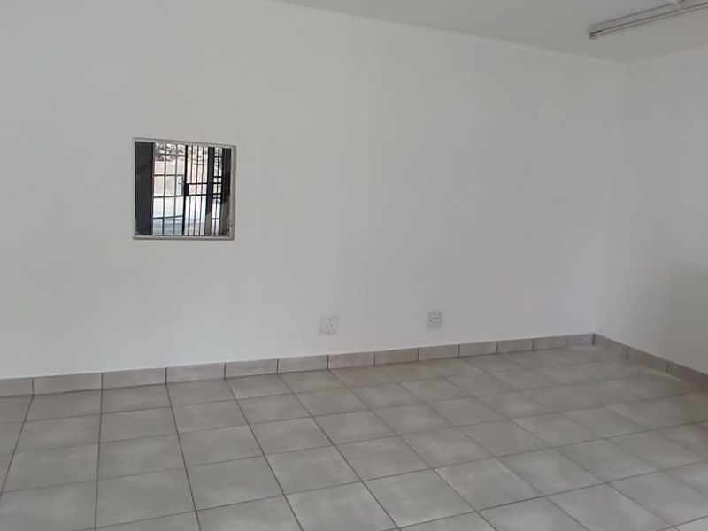A clean, empty open-plan industrial space featuring neutral tiled flooring, white walls, and secure window bars, suitable for various commercial or office uses.