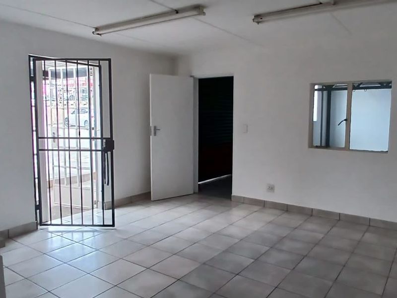 An empty open-plan industrial space featuring tiled flooring, fluorescent lighting, and a security gate, suitable for office or commercial use.