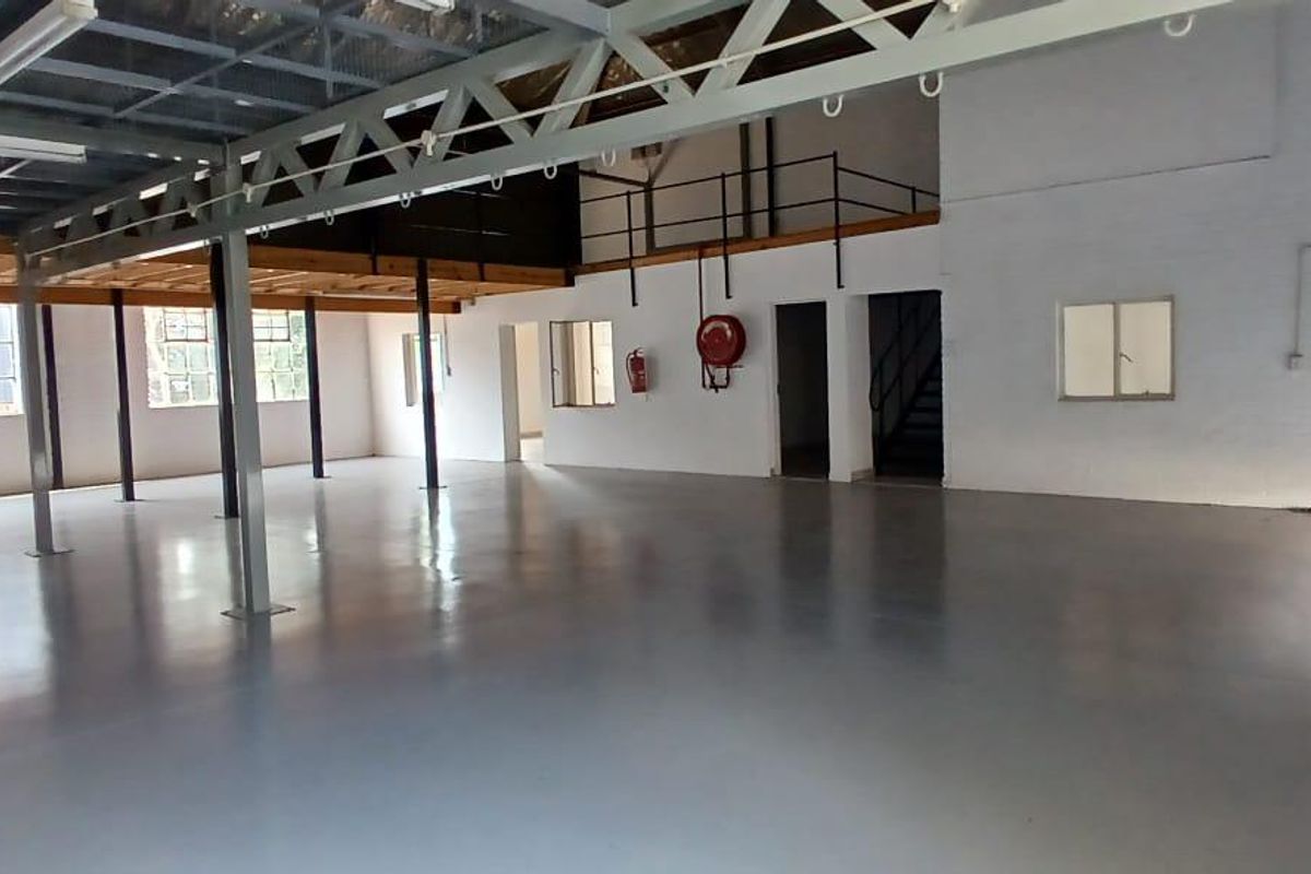 Spacious industrial warehouse unit featuring a mezzanine level, high ceilings with exposed steel trusses, polished epoxy flooring, and secure access points.