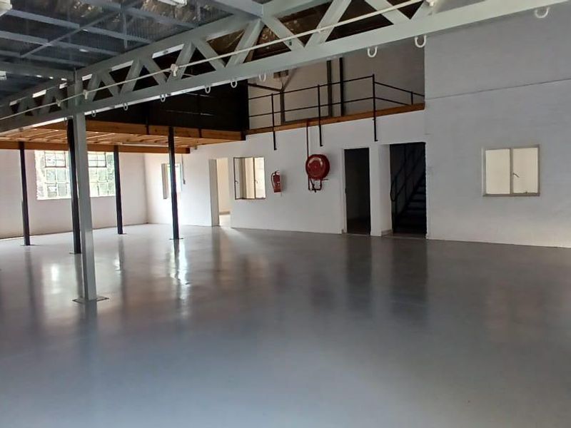 Spacious industrial warehouse unit featuring a mezzanine level, high ceilings with exposed steel trusses, polished epoxy flooring, and secure access points.