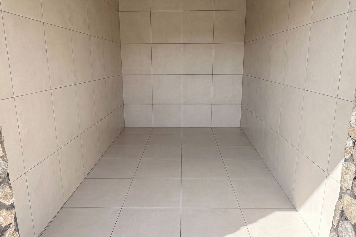 A clean, empty utility space featuring neutral floor-to-ceiling tiling and decorative stone-clad pillars at the entrance.