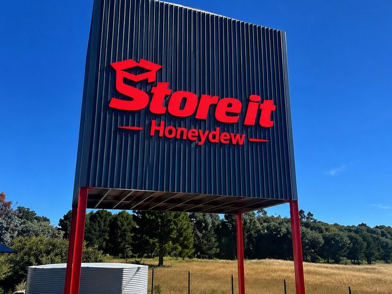 A prominent commercial signage structure for Store It Honeydew, featuring modern metal cladding and steel support columns set against a clear sky.