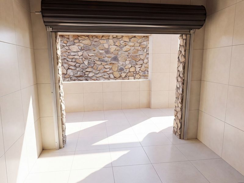 A clean, modern garage space featuring neutral tiled walls and flooring, stone-clad pillars, and a functional roller shutter door opening to an outdoor area.