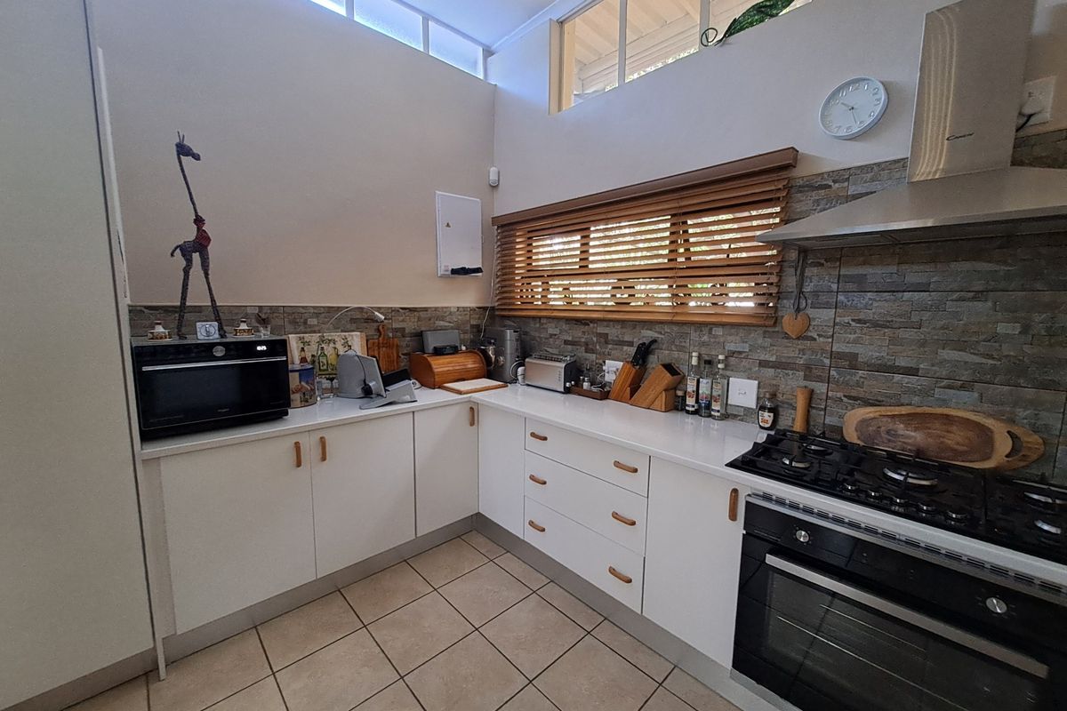 A well-maintained kitchen featuring white cabinetry, stone countertops, a gas hob with extractor fan, and a stone tile backsplash with clerestory windows.