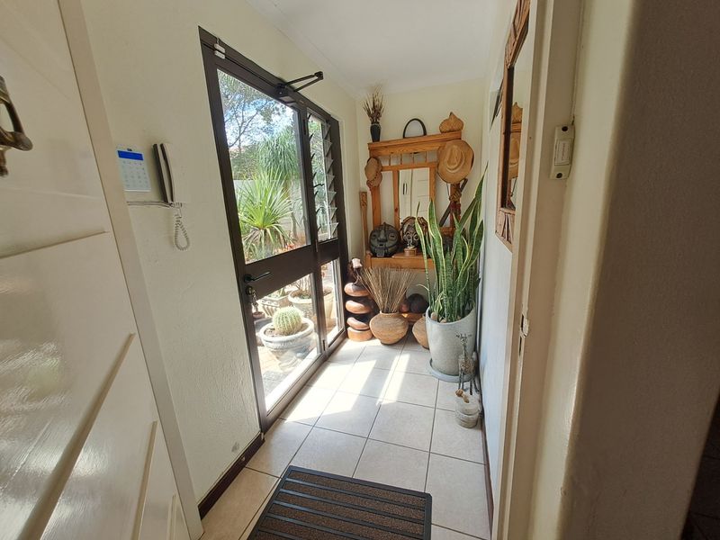 A bright entrance hall featuring tiled flooring and a glass-panelled door with security gate, providing direct access to the outdoor area.