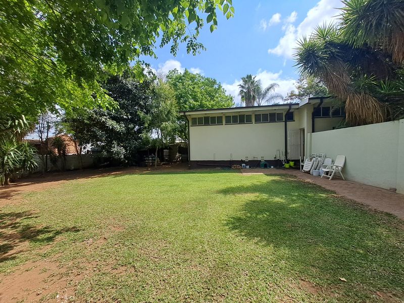 A spacious rear garden featuring a large lawn, paved walkway, and boundary wall, providing a private outdoor area for the property.