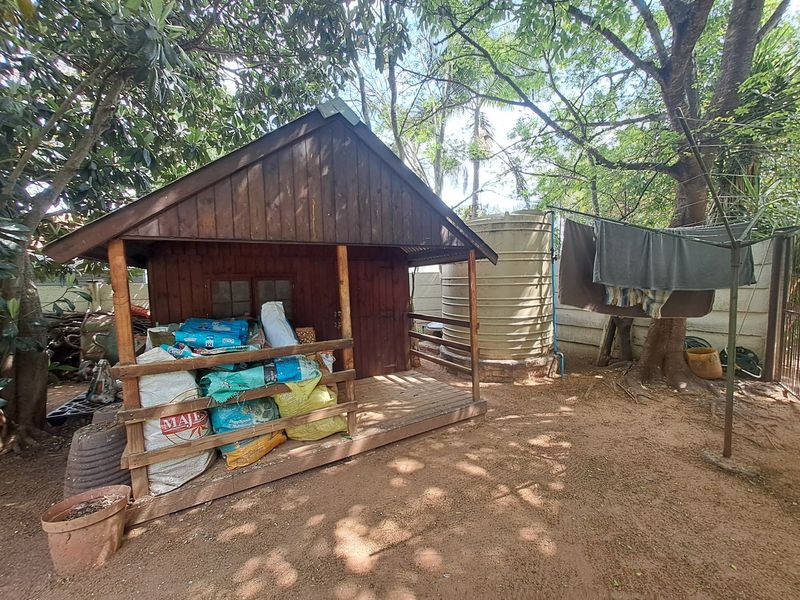 A garden area featuring a wooden storage shed, a large water tank, and a rotary clothesline set within a shaded, unpaved outdoor space.