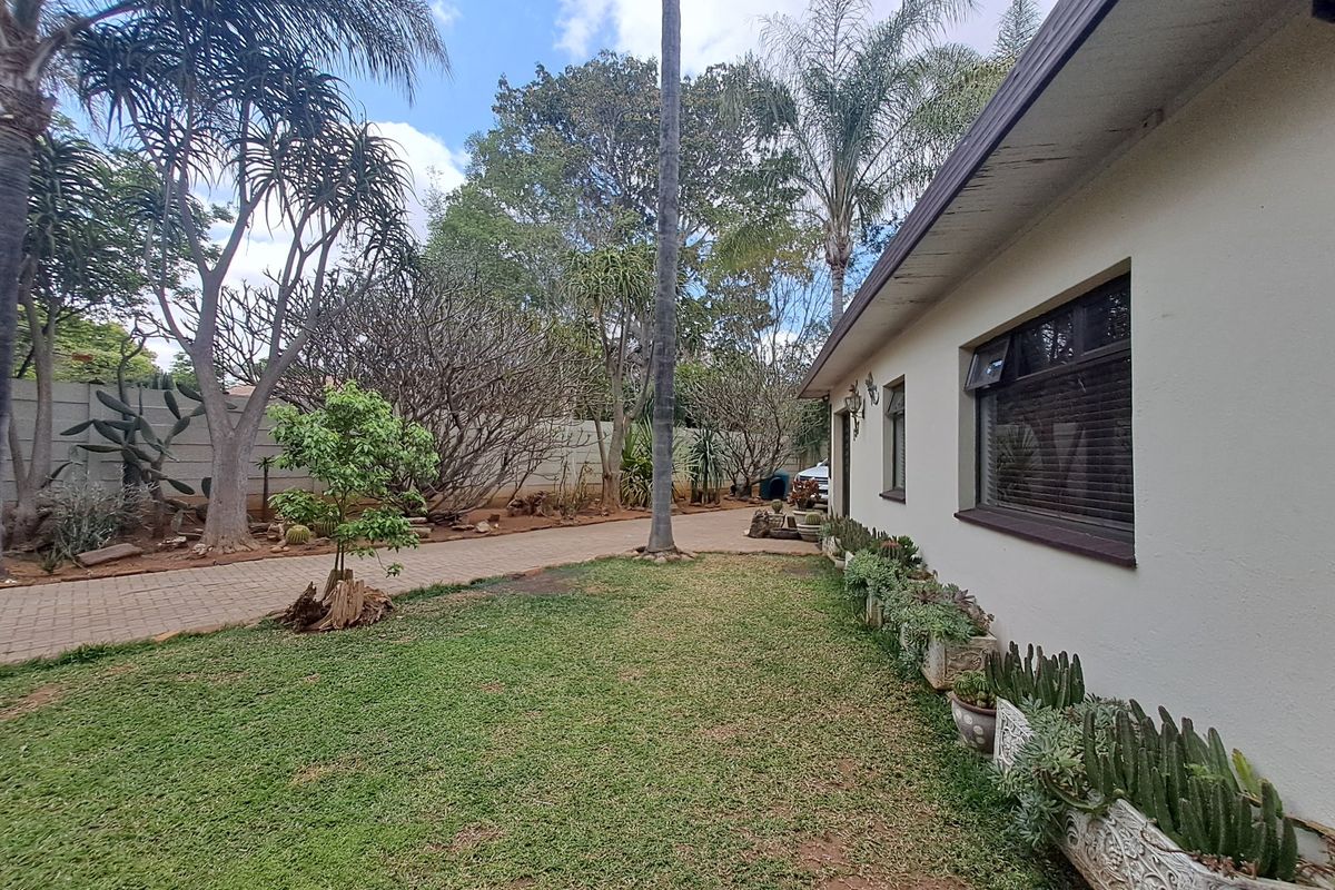 A view of the rear garden featuring a well-maintained lawn, paved driveway, and established landscaping along the boundary wall.