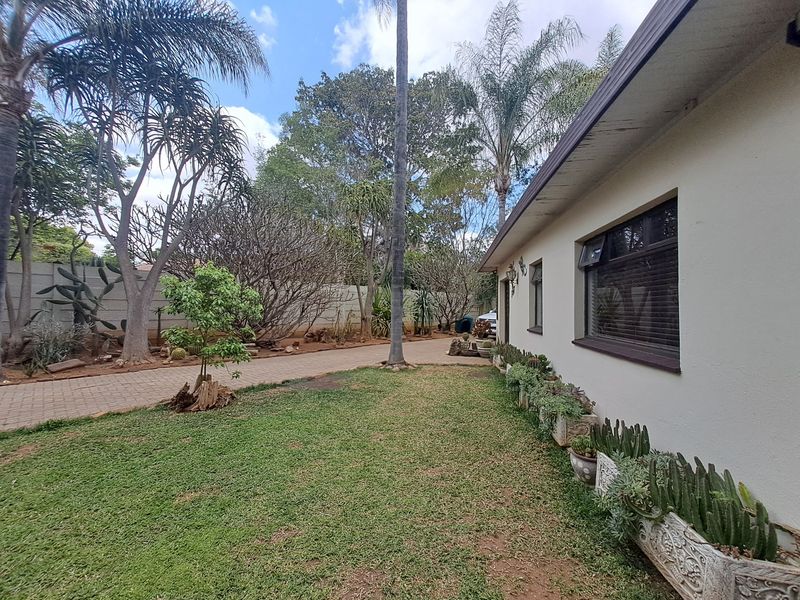 A view of the rear garden featuring a well-maintained lawn, paved driveway, and established landscaping along the boundary wall.