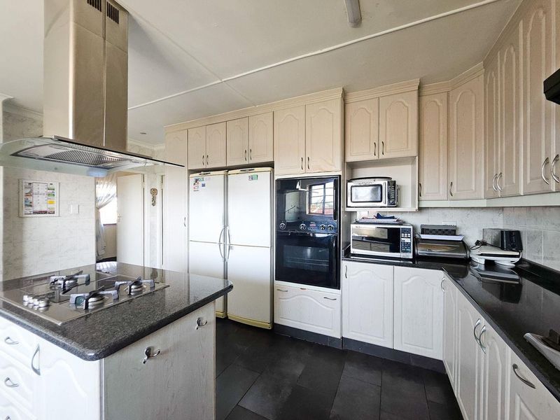 A functional kitchen featuring granite countertops, a central island with a gas hob, built-in oven, and ample cabinetry storage.