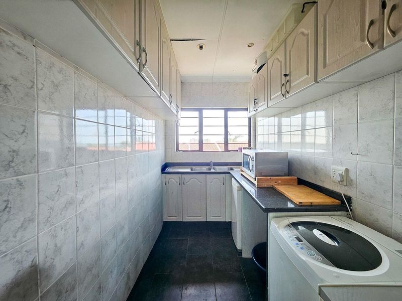 A functional scullery area featuring built-in cabinetry, granite countertops, a double sink, and tiled splashbacks, requiring some ceiling repairs.