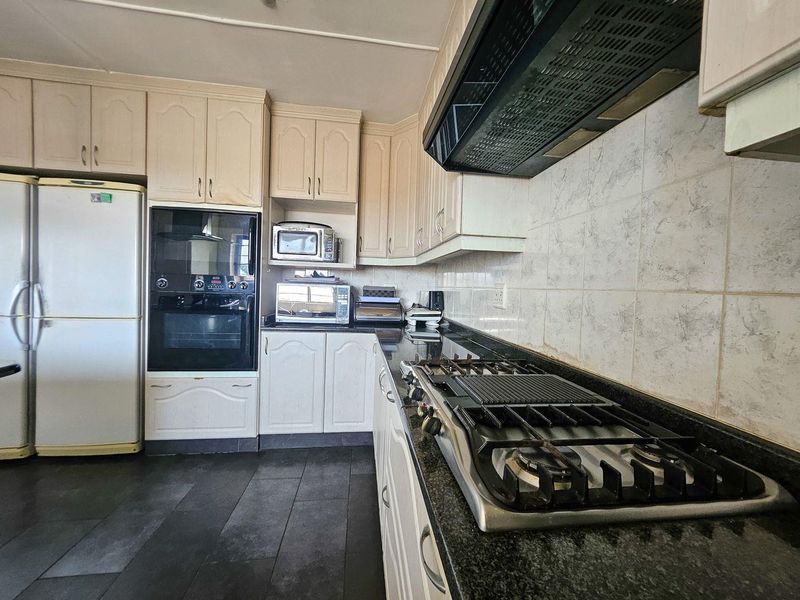 A functional kitchen featuring built-in cabinetry, granite countertops, a gas hob with extractor fan, and a built-in oven, finished with tiled flooring and backsplash.