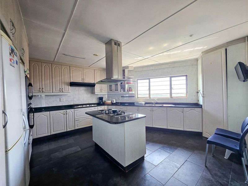 Spacious kitchen featuring a central island with gas hob, ample built-in cabinetry, double sink, and tiled flooring throughout.