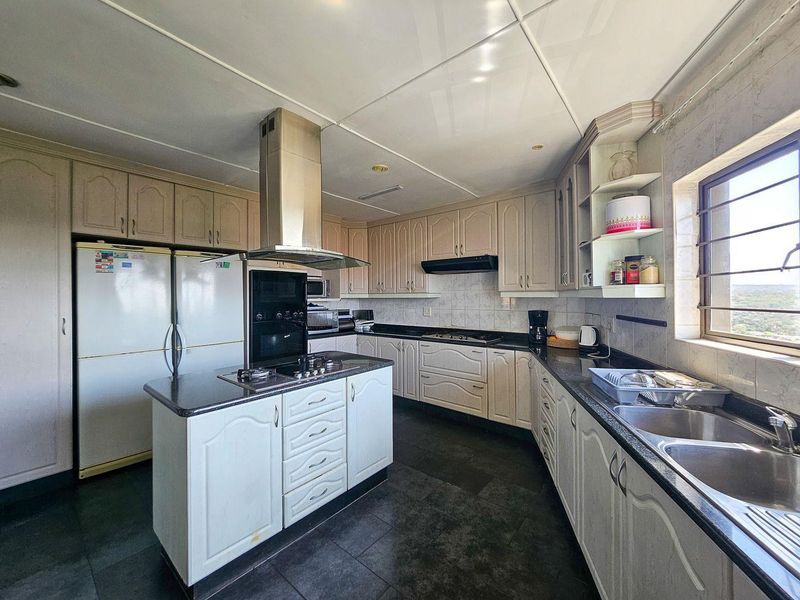 Spacious kitchen featuring a central island with a gas hob, granite countertops, ample built-in cabinetry, and a stainless steel extractor fan.