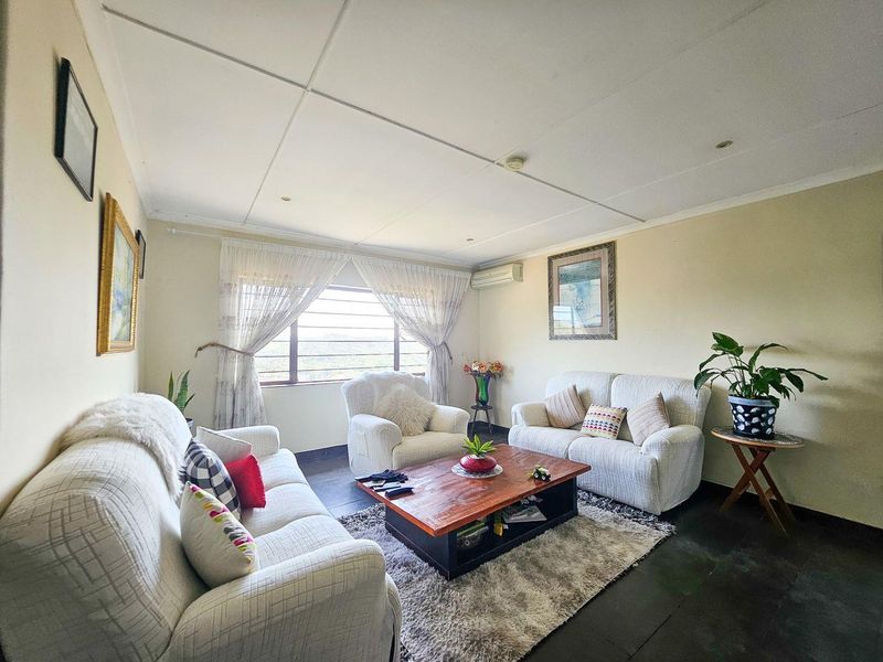 A comfortable living room featuring tiled flooring, a wall-mounted air conditioning unit, and large windows with security bars.