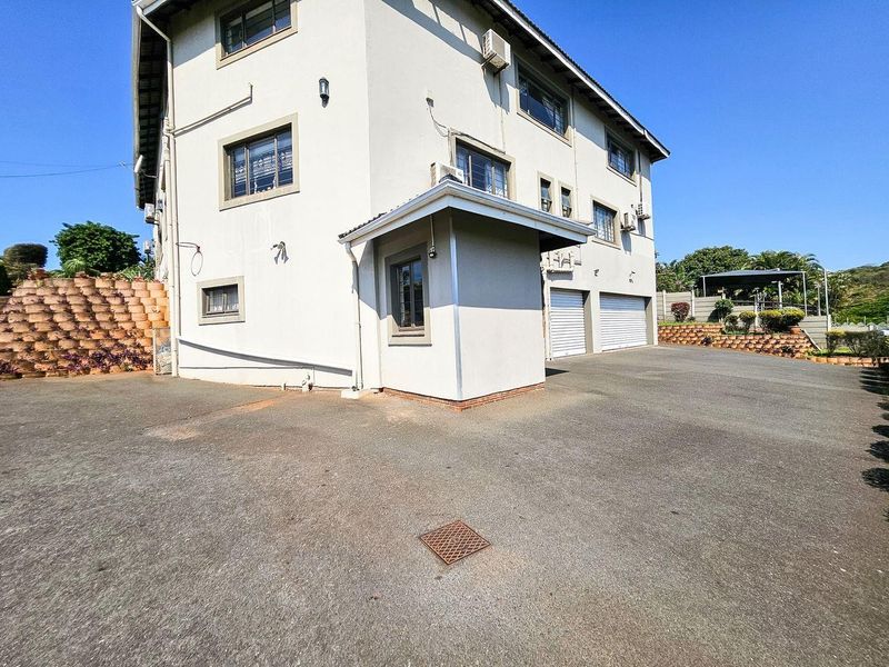 Exterior view of a multi-story house featuring a paved driveway, double garage, and retaining wall structure.