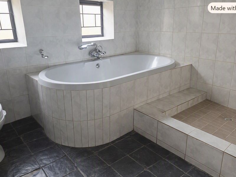 A functional bathroom featuring a built-in bathtub, a tiled shower area, and neutral wall tiling with contrasting dark floor tiles.