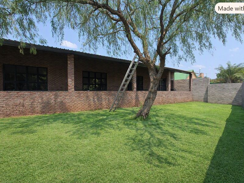 A spacious rear garden featuring a well-maintained lawn, a covered patio with face brick finishes, and black framed windows.