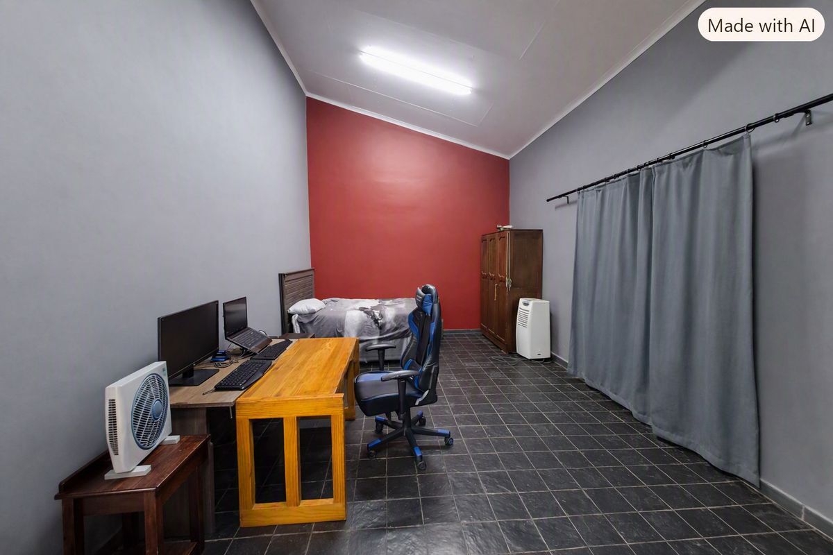 A bedroom featuring dark tiled flooring, a vaulted ceiling, and a bold red accent wall, currently utilized as a multi-purpose living and workspace.