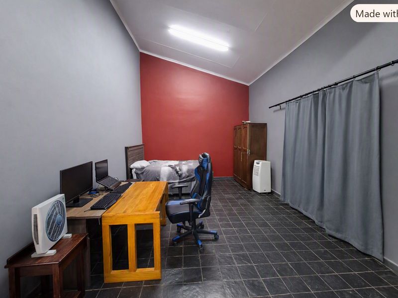 A bedroom featuring dark tiled flooring, a vaulted ceiling, and a bold red accent wall, currently utilized as a multi-purpose living and workspace.