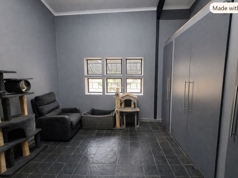 A bedroom featuring dark tiled flooring, built-in cupboards, and windows fitted with security bars.