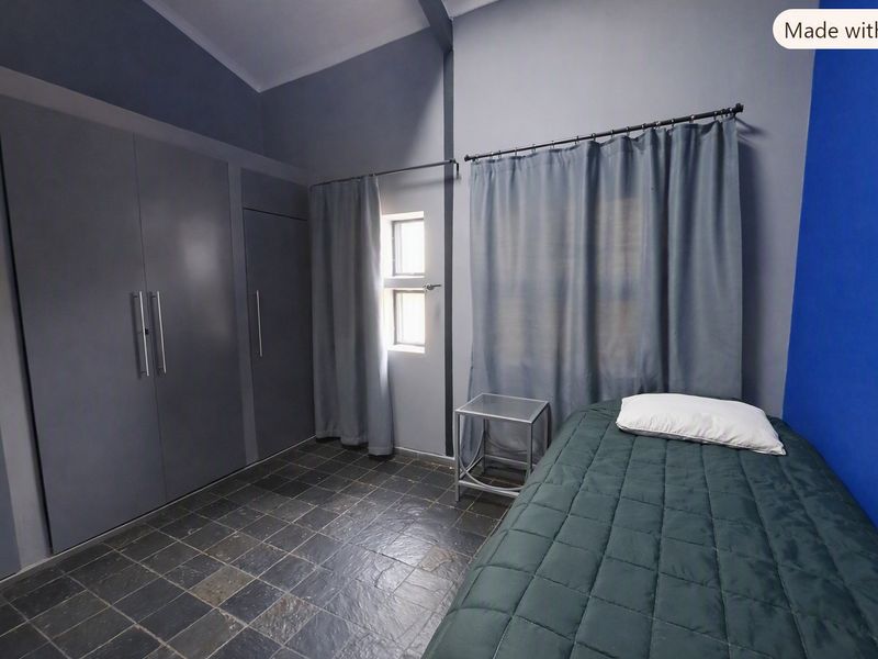 A bedroom featuring built-in cupboards, dark tiled flooring, and a vaulted ceiling with a modern blue accent wall.