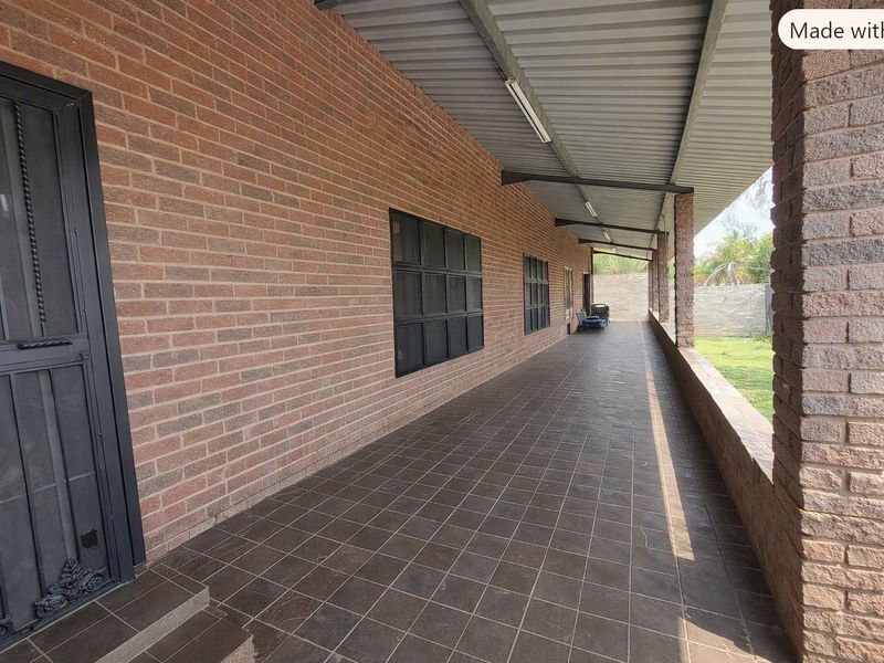 A covered outdoor patio featuring brick walls, tiled flooring, and structural brick pillars, providing a functional space overlooking the garden area.