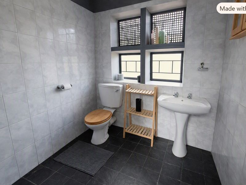 A functional bathroom featuring a pedestal basin, toilet, and neutral tiled finishes with natural light from a window with security bars.