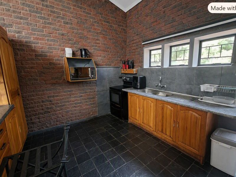 A kitchen featuring exposed brick walls, wooden cabinetry, a stainless steel sink, and a freestanding stove with tiled flooring.