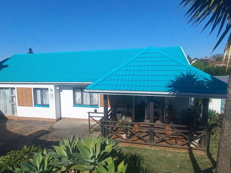 Front elevation of a residential house featuring a distinctive blue metal roof, a covered patio with timber balustrade, and paved entrance area.