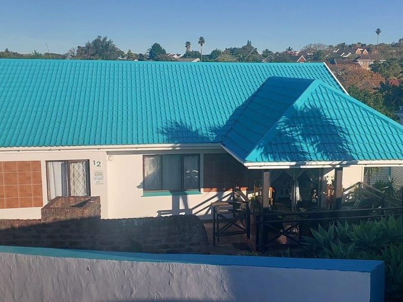 Front elevation of a residential house featuring a distinctive bright blue metal roof, covered patio area, and brick boundary wall.
