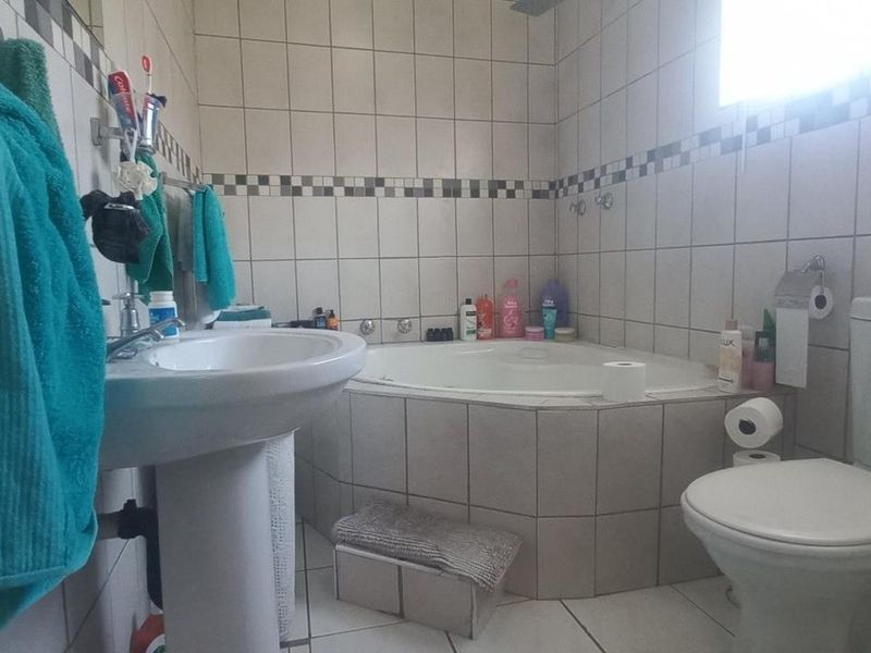 A functional bathroom featuring a corner bathtub, pedestal basin, and toilet with neutral wall and floor tiling.