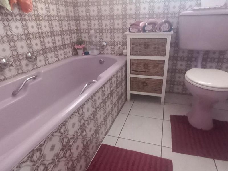 A dated bathroom featuring a pink bathtub and toilet suite with patterned wall tiles and white floor tiles.