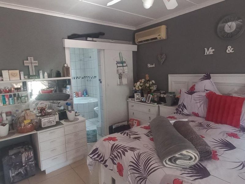 A bedroom featuring tiled flooring, a ceiling fan, an air conditioning unit, and an adjoining en-suite bathroom with a sliding door entrance.