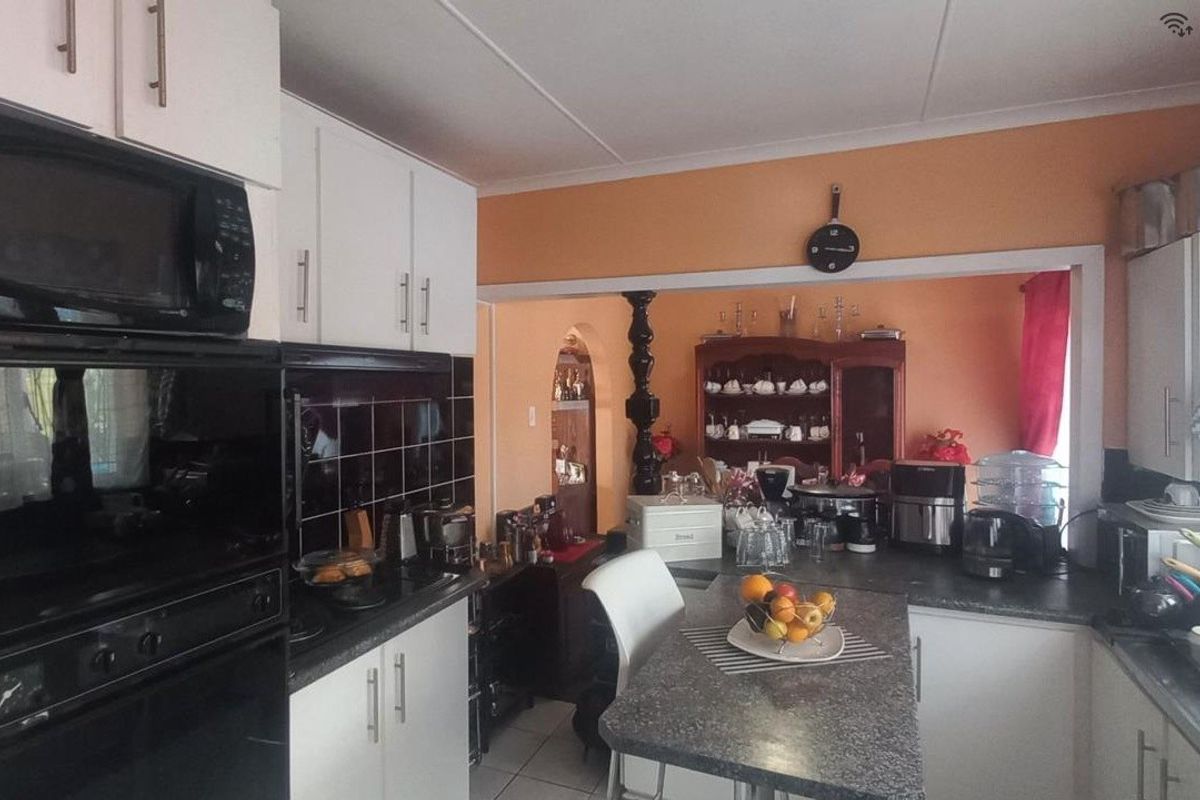 A functional kitchen featuring built-in appliances, dark tiled backsplash, laminate countertops, and a breakfast bar, opening into an adjacent living area.