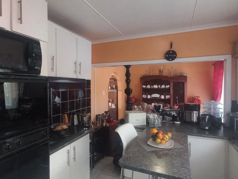 A functional kitchen featuring built-in appliances, dark tiled backsplash, laminate countertops, and a breakfast bar, opening into an adjacent living area.