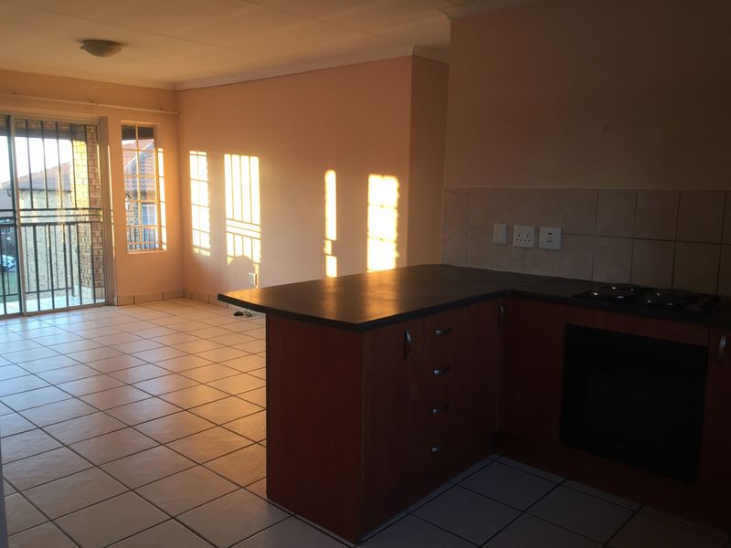 Open-plan living area featuring a functional kitchen with built-in cabinetry, oven, and hob, leading to a balcony with security bars.