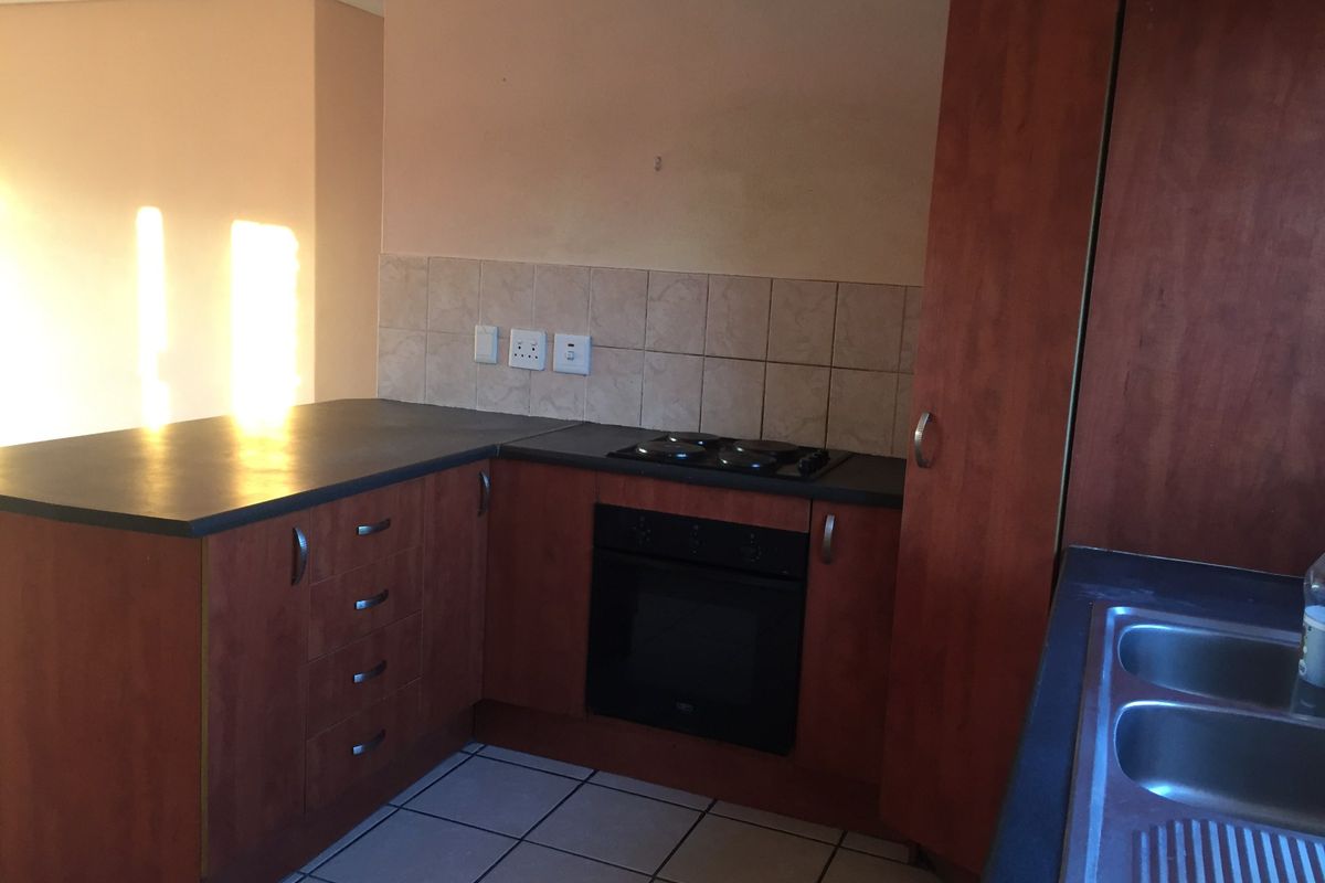 A functional kitchen featuring wood-tone cabinetry, dark laminate countertops, a built-in oven and hob, and a double bowl sink with tiled backsplash.