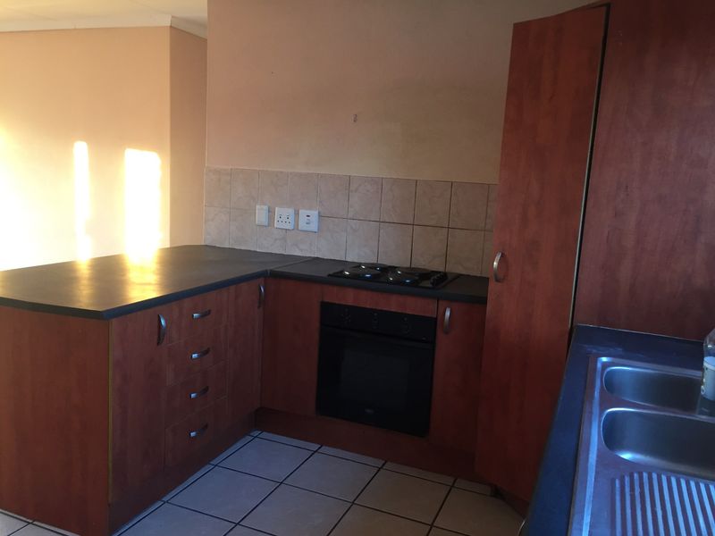 A functional kitchen featuring wood-tone cabinetry, dark laminate countertops, a built-in oven and hob, and a double bowl sink with tiled backsplash.