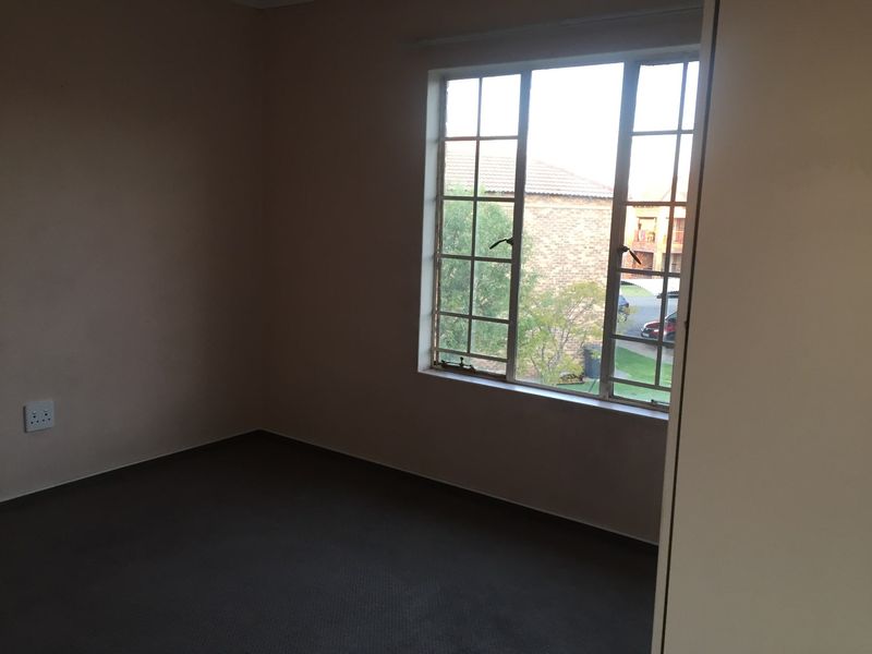 An empty bedroom featuring carpeted flooring and a large window providing natural light and a view of the surrounding complex.