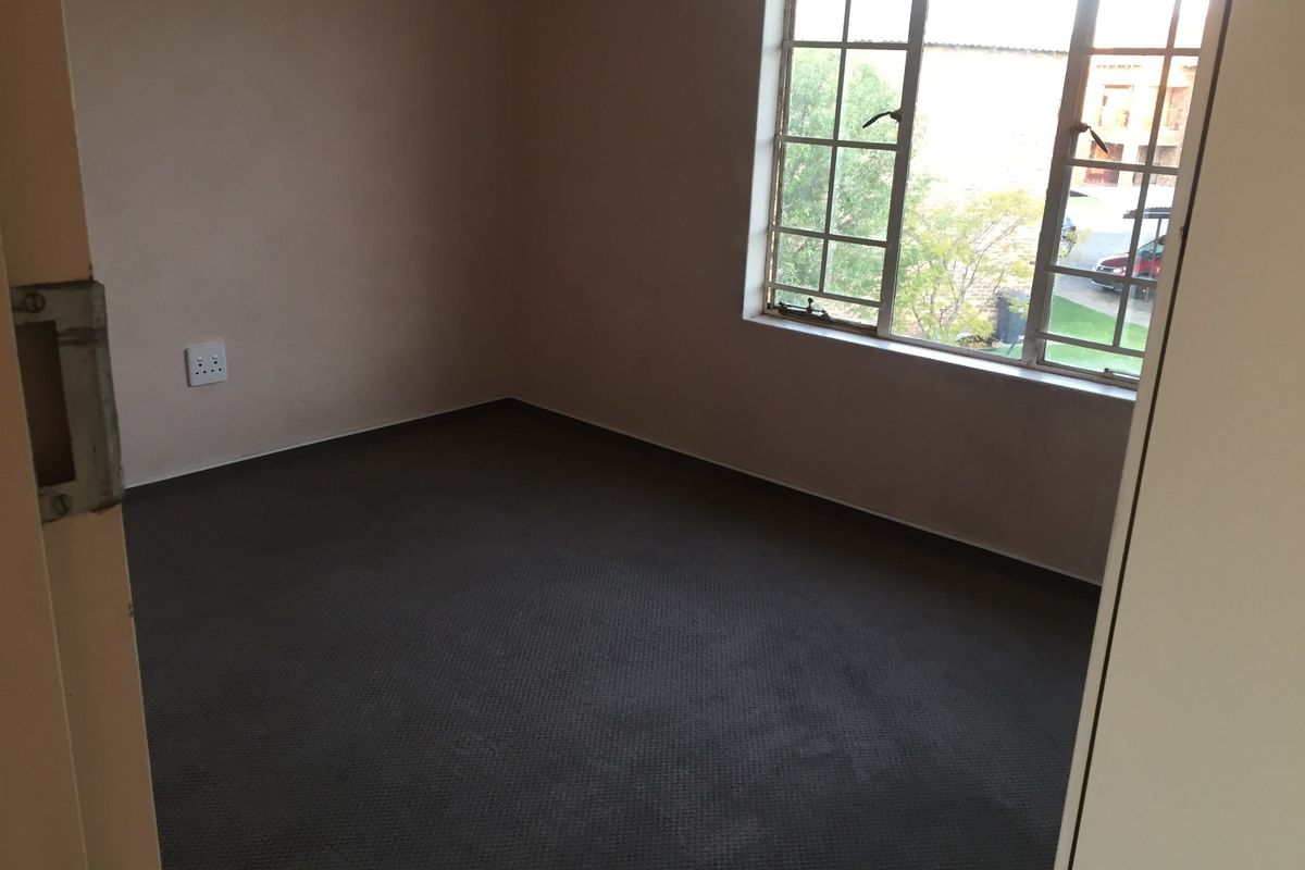 An empty bedroom featuring carpeted flooring and a large grid-pattern window providing natural light.