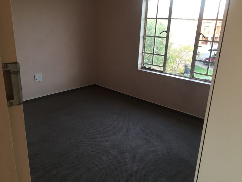 An empty bedroom featuring carpeted flooring and a large grid-pattern window providing natural light.