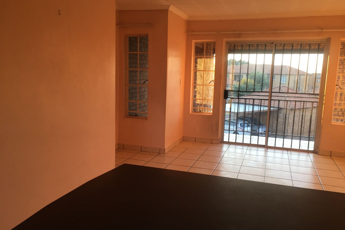 An empty living area featuring tiled flooring, large windows, and a sliding glass door with security bars leading to an outdoor space.