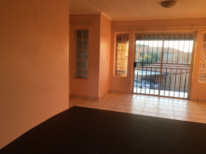An empty living area featuring tiled flooring, large windows, and a sliding glass door with security bars leading to an outdoor space.