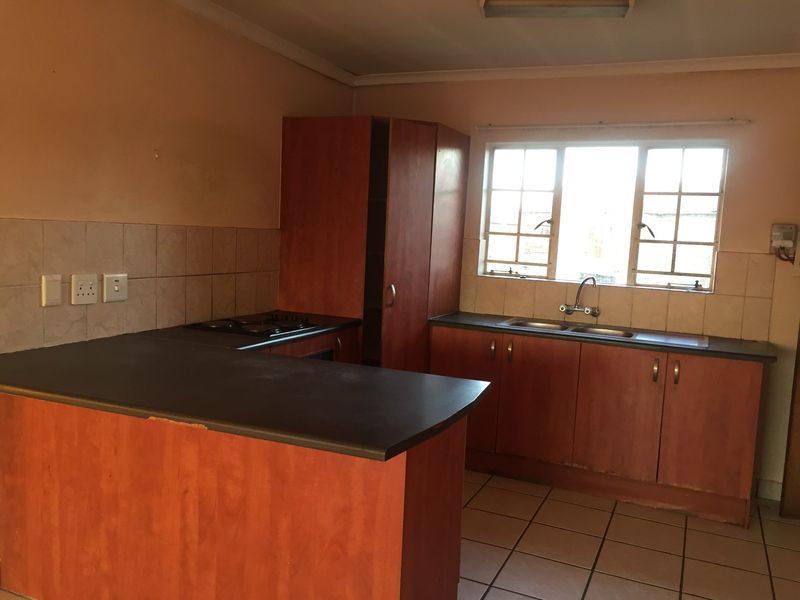 A dated kitchen featuring laminate cabinetry, a double basin sink, built-in hob, and tiled flooring, offering a functional layout ready for modernization.