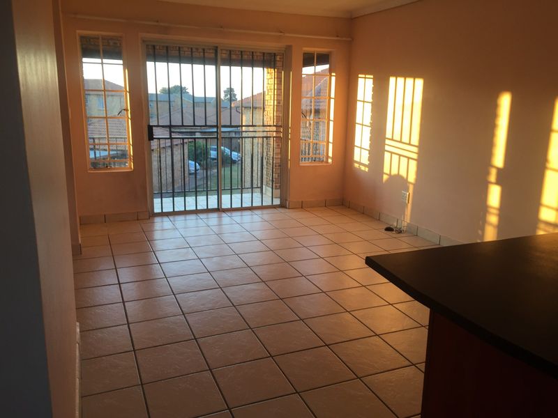 An empty open-plan living area featuring tiled flooring, a sliding glass door with security gate, and natural light streaming through the windows.