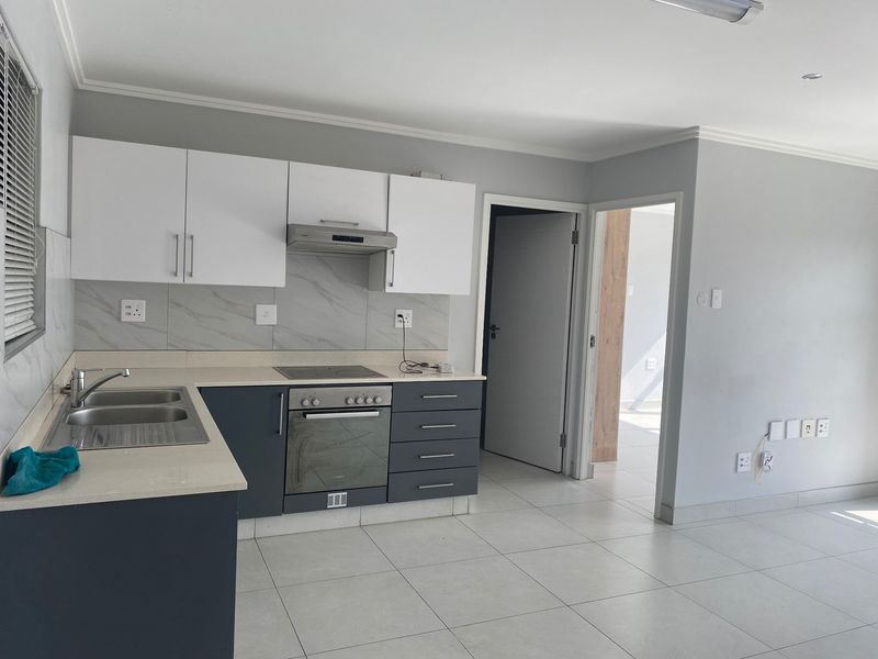Modern kitchen featuring white and dark grey cabinetry, stone countertops, integrated oven and hob, and neutral tiled flooring in an open-plan layout.