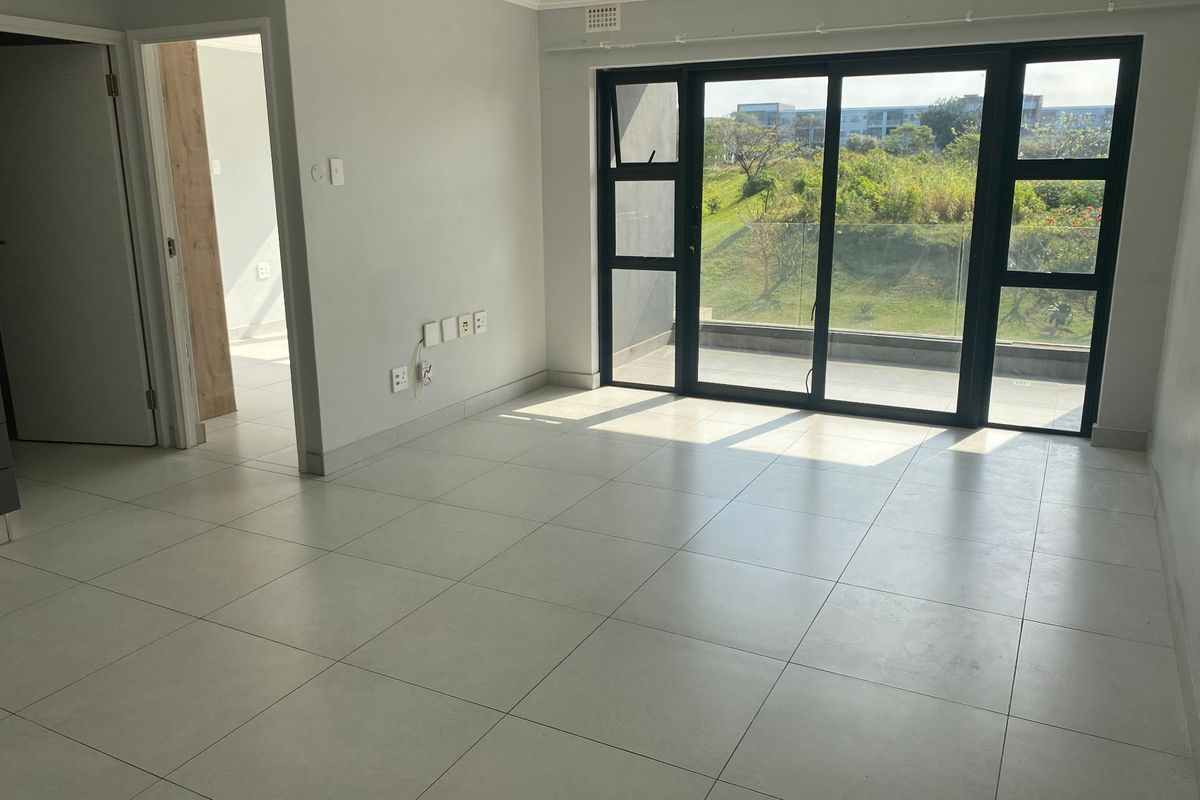 A bright, empty living area featuring large sliding glass doors that open to a balcony, complemented by neutral tiled flooring and clean finishes.