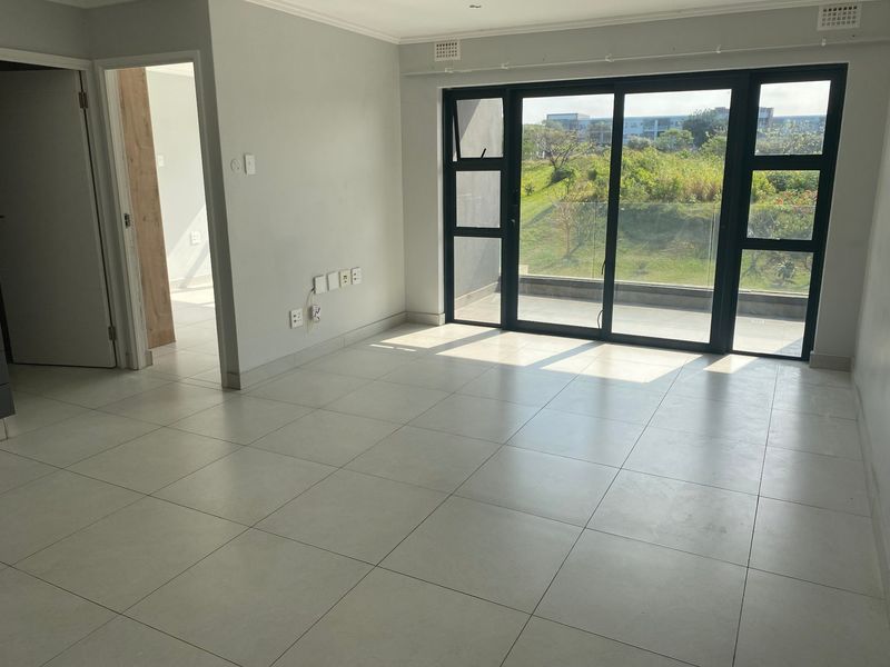 A bright, empty living area featuring large sliding glass doors that open to a balcony, complemented by neutral tiled flooring and clean finishes.